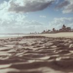 Praia de Cumbuco, no Ceará, com faixa de areia, coqueiros e céu nublado.