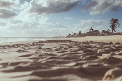 Praia de Cumbuco, no Ceará, com faixa de areia, coqueiros e céu nublado.