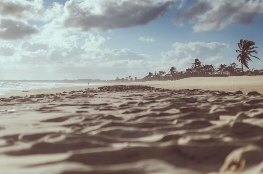 Praia de Cumbuco, no Ceará, com faixa de areia, coqueiros e céu nublado.