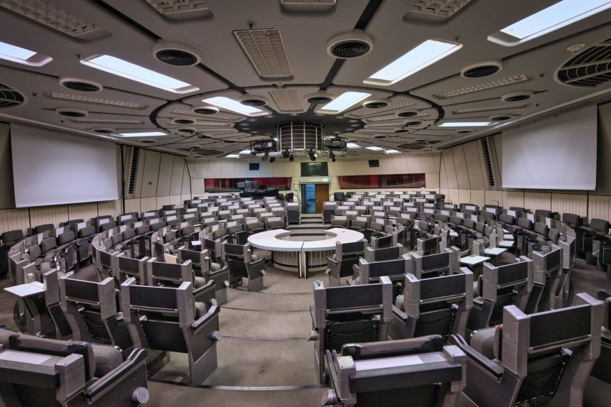 Sala de conferências futurista, vazia, com assentos circulares e elementos de design de alta tecnologia.