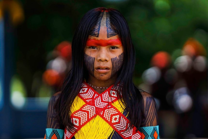 Retrato de uma mulher indígena em ambiente amazônico, com vegetação ao fundo